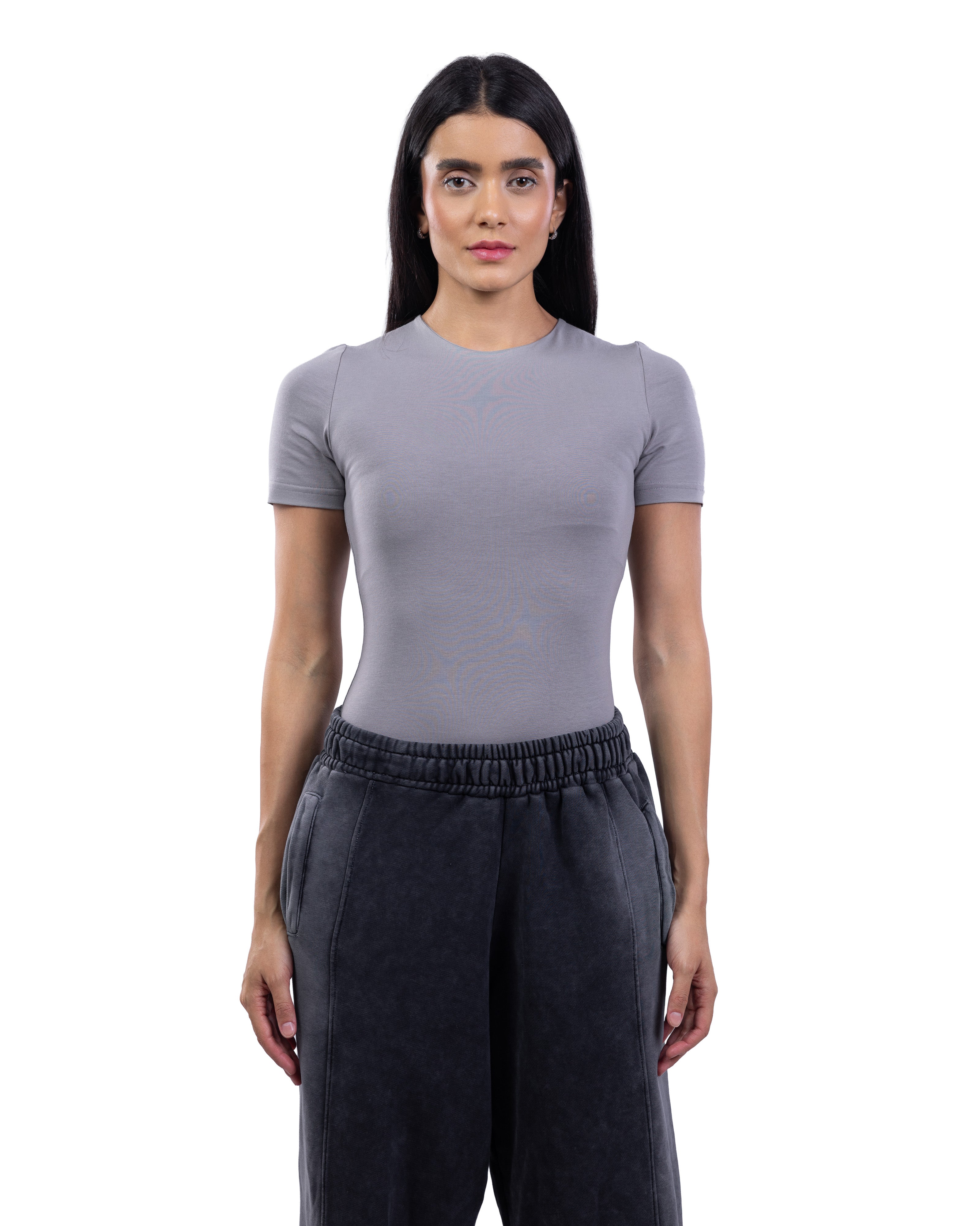 A woman modeling a fitted short-sleeve crewneck top in light gray, paired with dark charcoal sweatpants, against a plain white background.