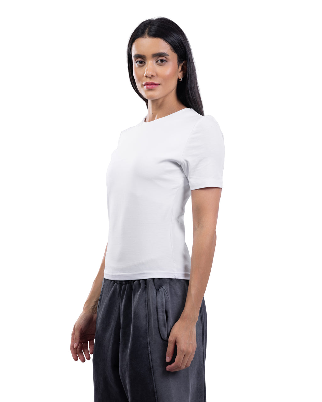 A woman modeling a plain white short-sleeve crewneck t-shirt paired with dark gray trousers, photographed against a seamless white background.