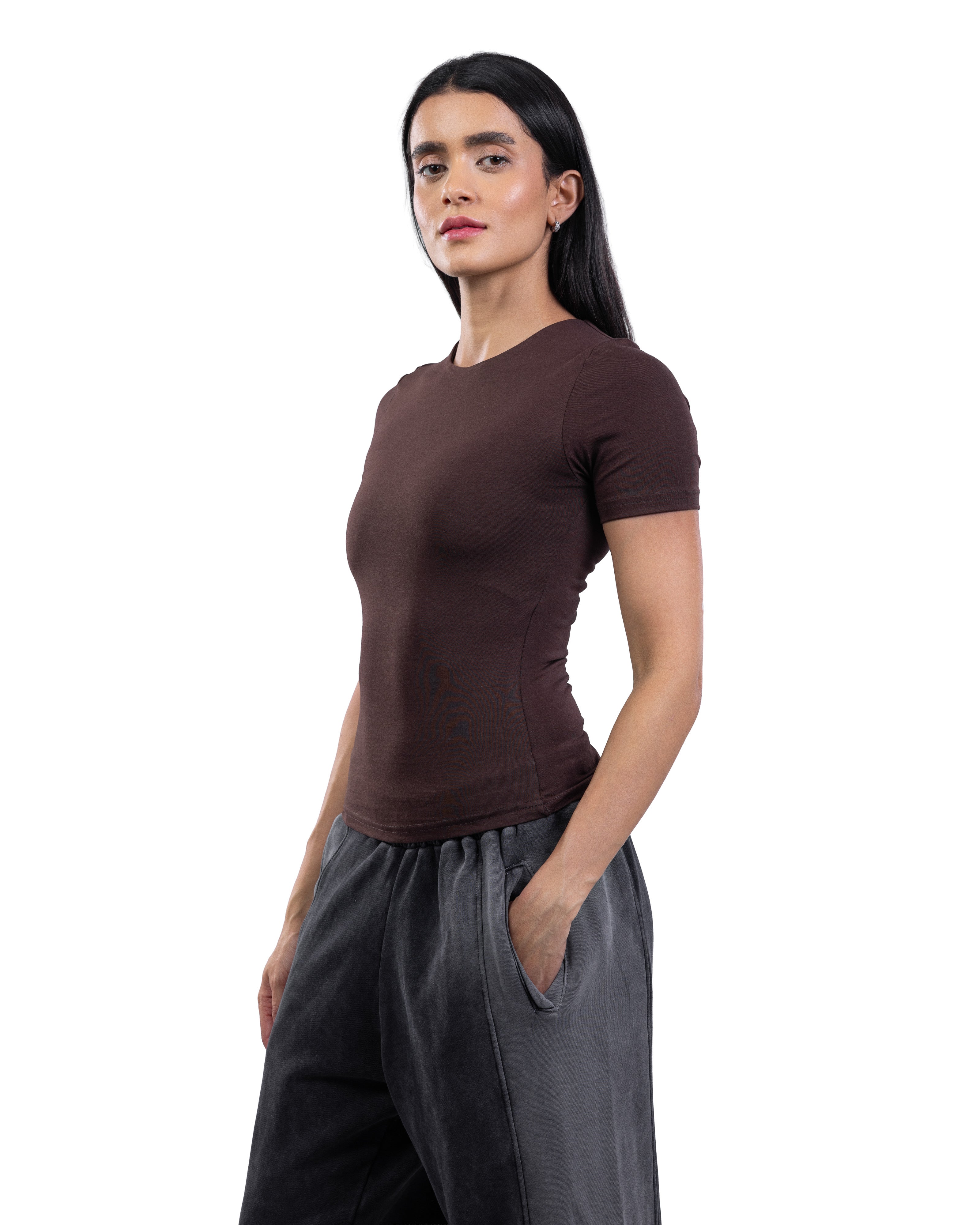 A woman modeling a fitted short-sleeve crewneck top in dark brown, paired with loose dark gray pants, against a plain white background.