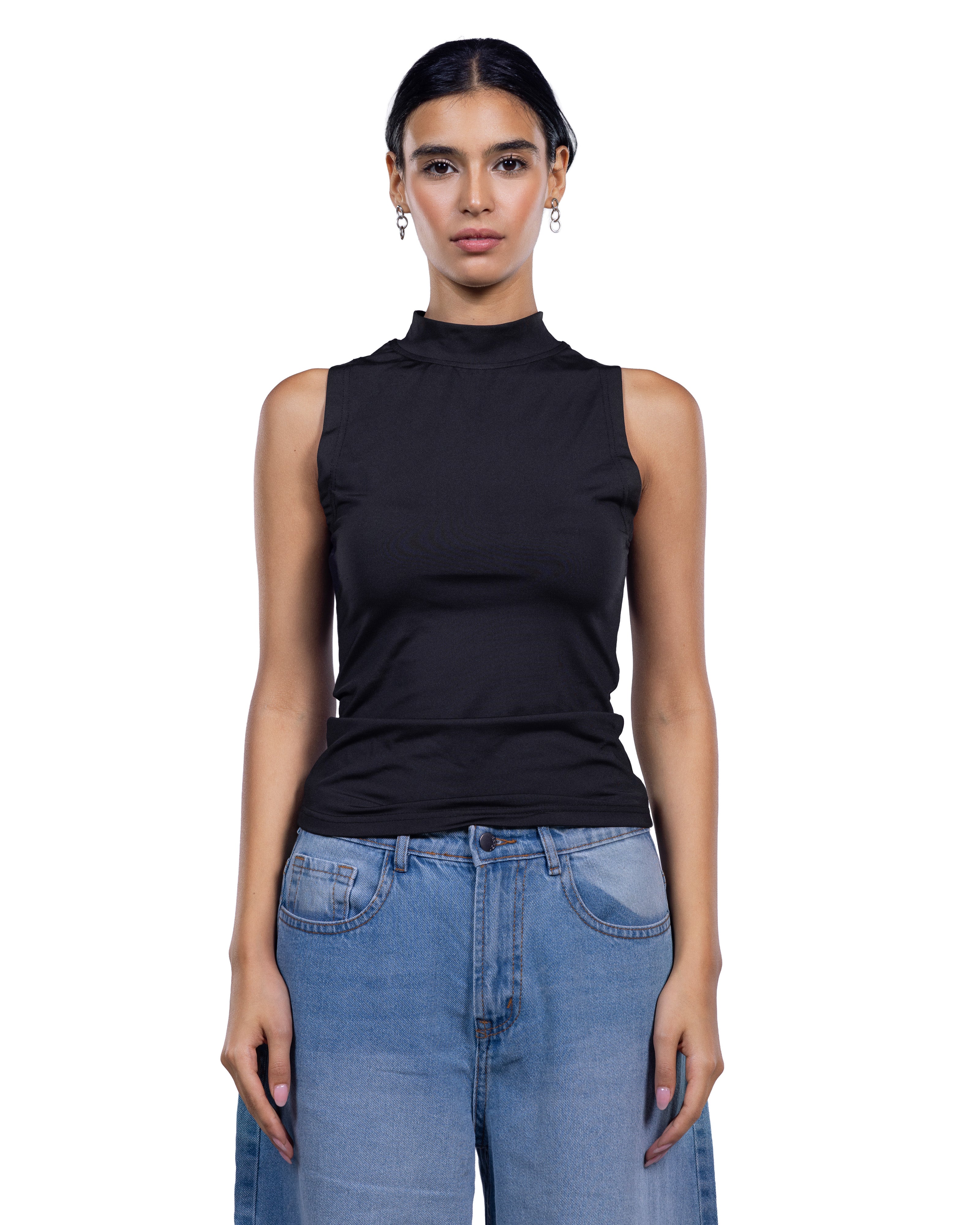 A woman modeling a sleeveless black mock neck top paired with light blue jeans against a plain white background.