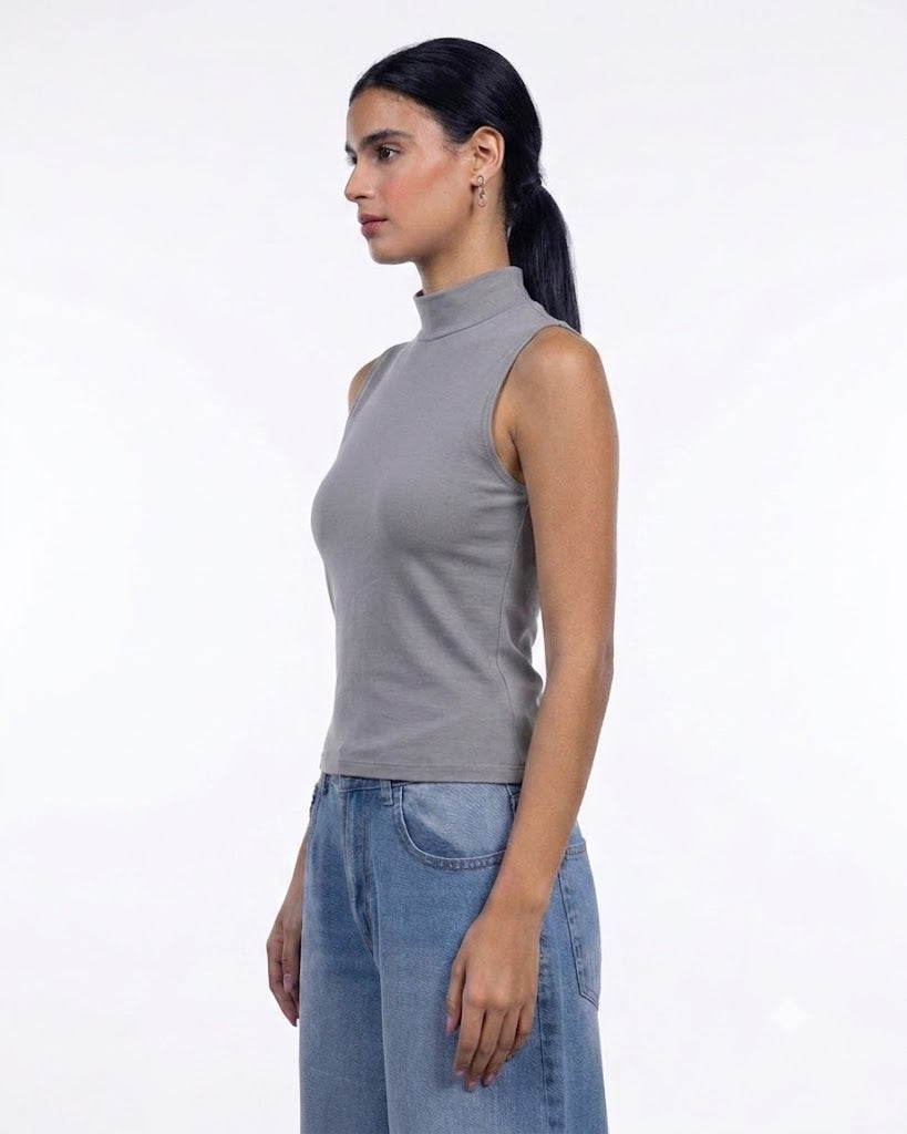 A woman in profile wearing a sleeveless gray mock neck top and light blue jeans, photographed against a clean white studio background.