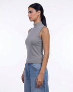 A woman in profile wearing a sleeveless gray mock neck top and light blue jeans, photographed against a clean white studio background. [model:1]