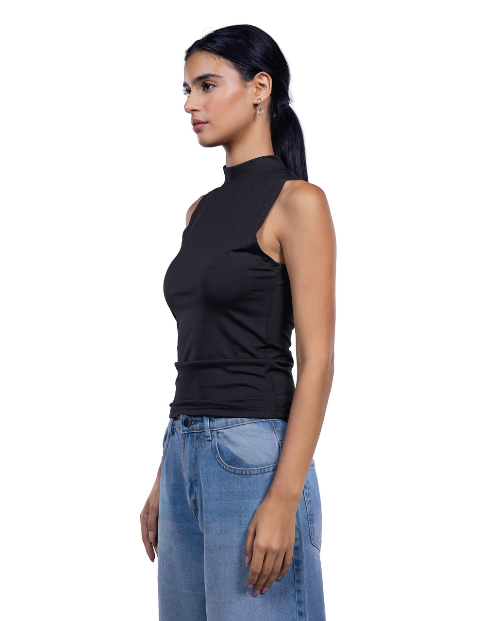 A woman shown in side profile wearing a fitted sleeveless black mock-neck top and light blue jeans against a plain white studio background.
