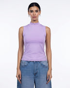 A woman modeling a sleeveless mock neck top in light purple/lavender, paired with blue jeans, against a plain white studio background. [model:1]