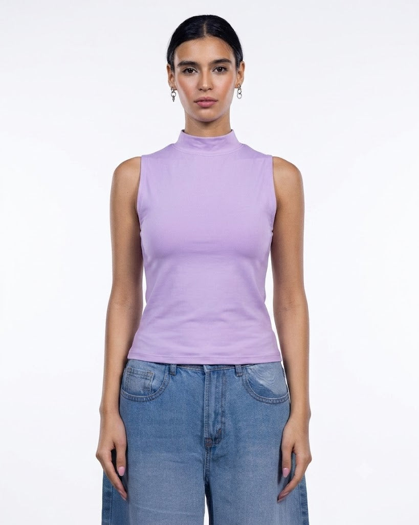 A woman modeling a sleeveless mock neck top in light purple/lavender, paired with blue jeans, against a plain white studio background.
