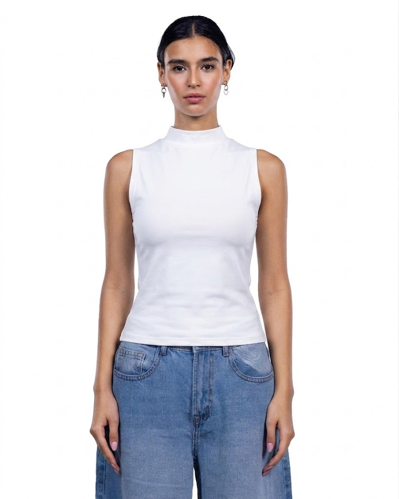 A woman modeling a white sleeveless mock neck top paired with light blue jeans against a plain white background.