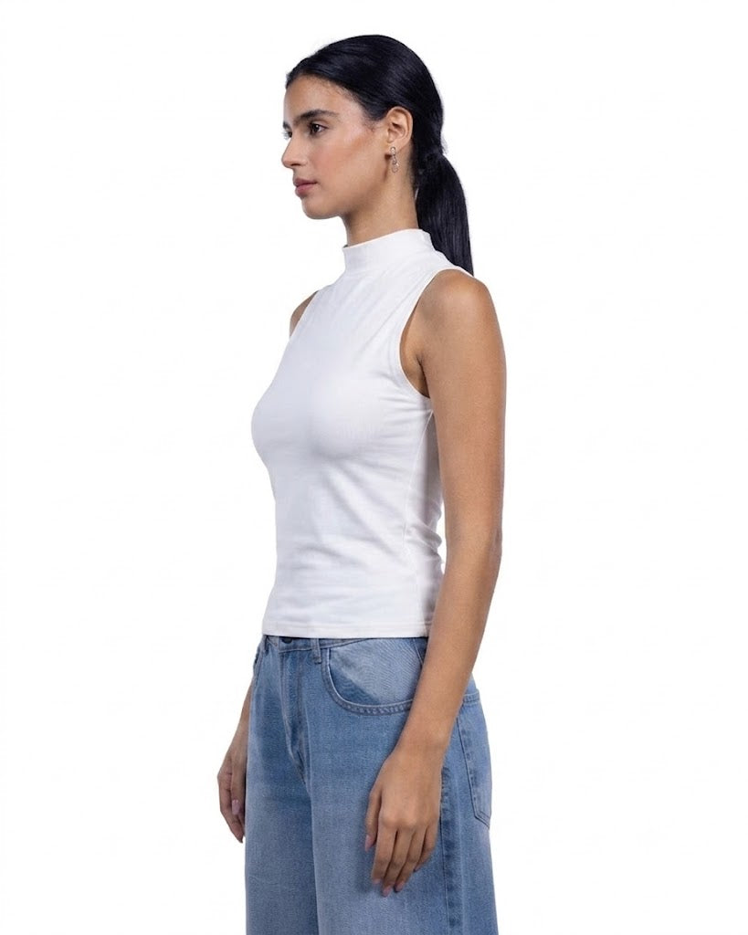 A woman in profile wearing a white sleeveless mock neck top and light blue jeans, photographed against a solid white background.