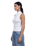A woman in profile wearing a white sleeveless mock neck top and light blue jeans, photographed against a solid white background. [model:1]