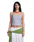 A woman modeling a light gray ribbed crop top with thin straps, paired with white pants and a green wrap, against a plain white background.