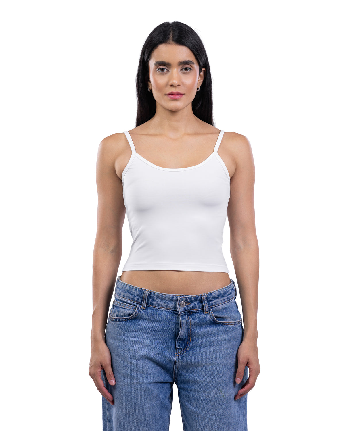 A woman modeling a white ribbed spaghetti-strap crop top with blue jeans against a plain white background.