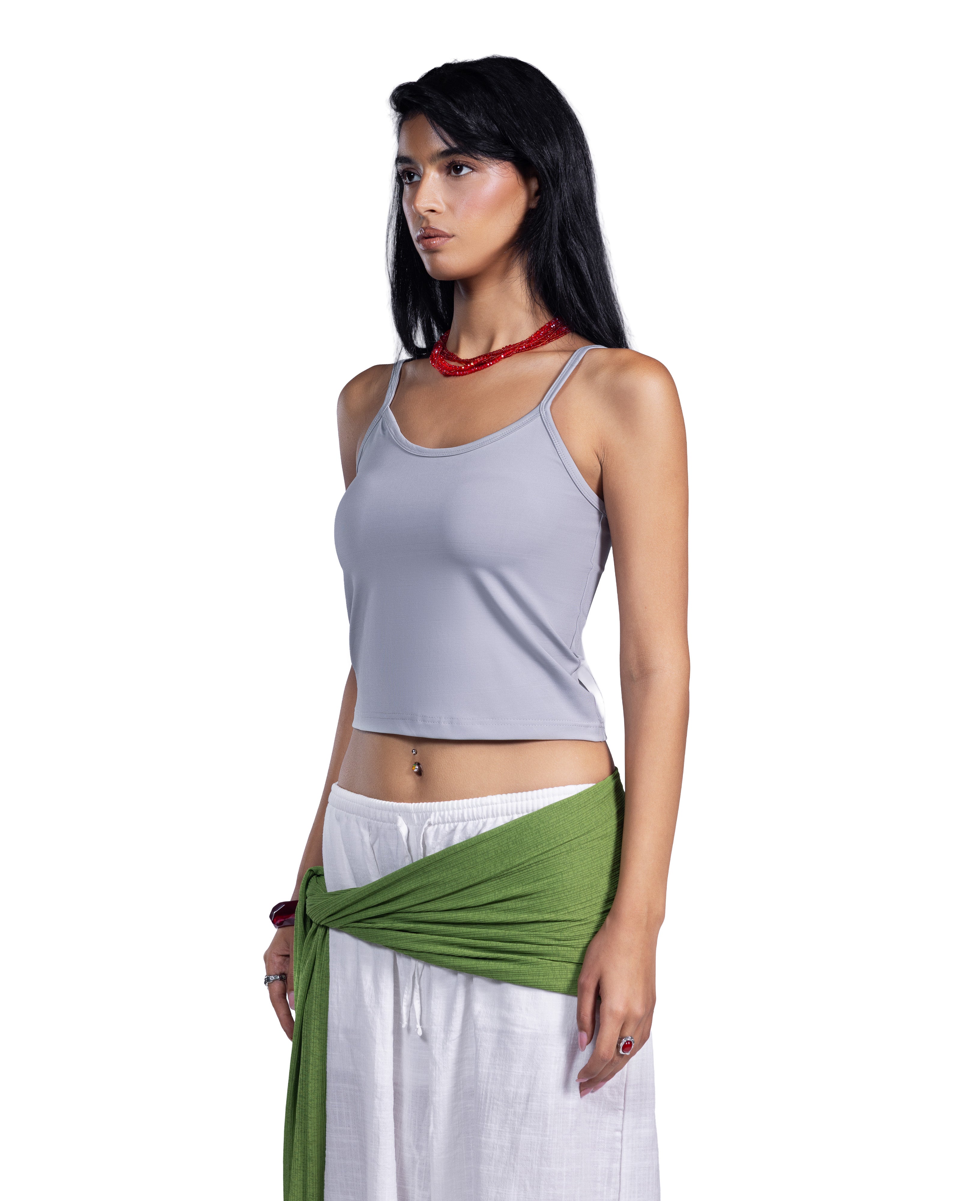 A woman modeling a light gray sleeveless crop top with white pants and a green wrap tied around her waist, against a plain white background.