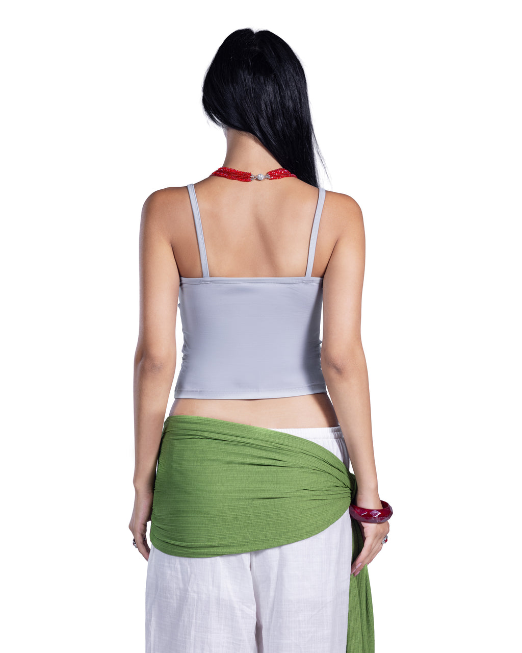 A woman shown from the back wearing a light gray spaghetti-strap crop top, white pants, and a green fabric wrap, against a plain white background.