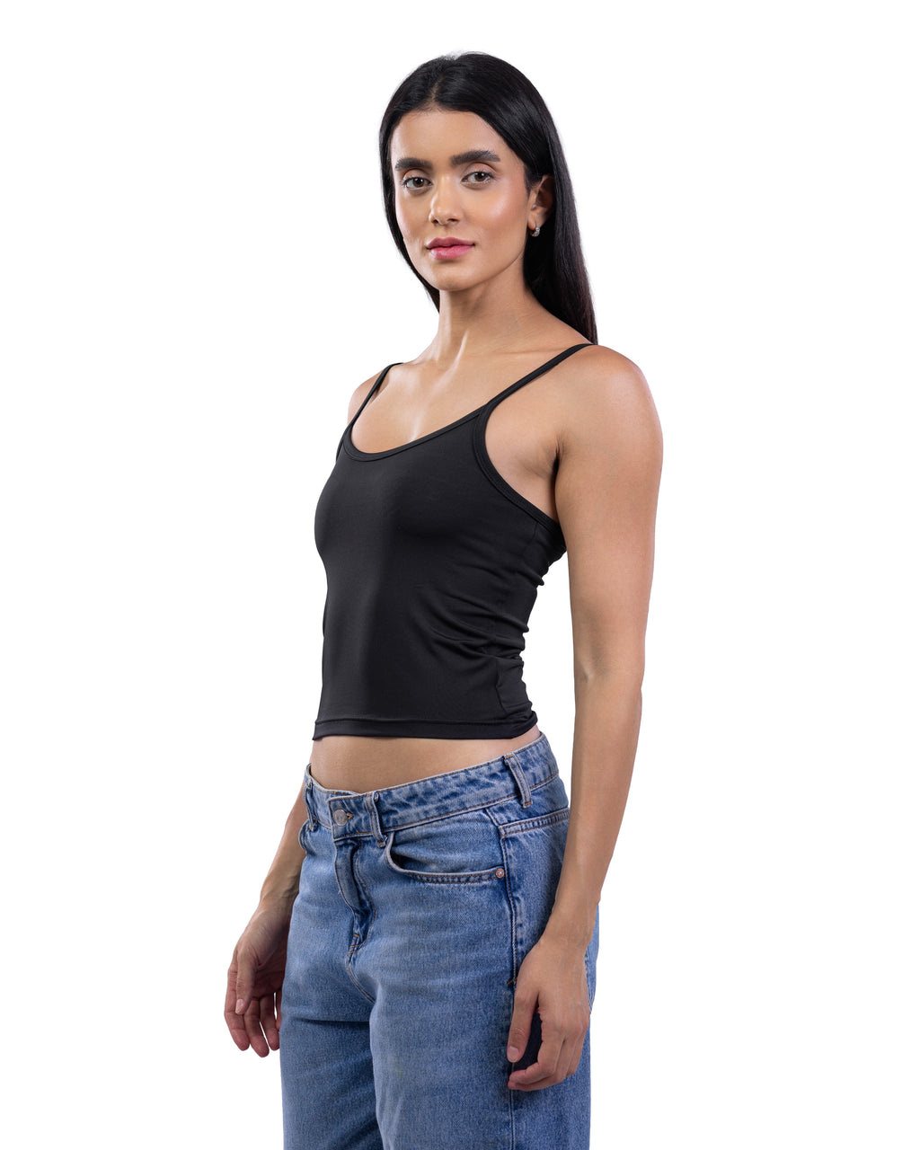 A woman modeling a black ribbed spaghetti-strap tank top paired with blue jeans, photographed against a solid white background.