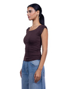 A woman shown in side profile wearing a fitted sleeveless scoop-neck top in dark brown and light-wash blue jeans, photographed against a plain white studio background. [model:1]