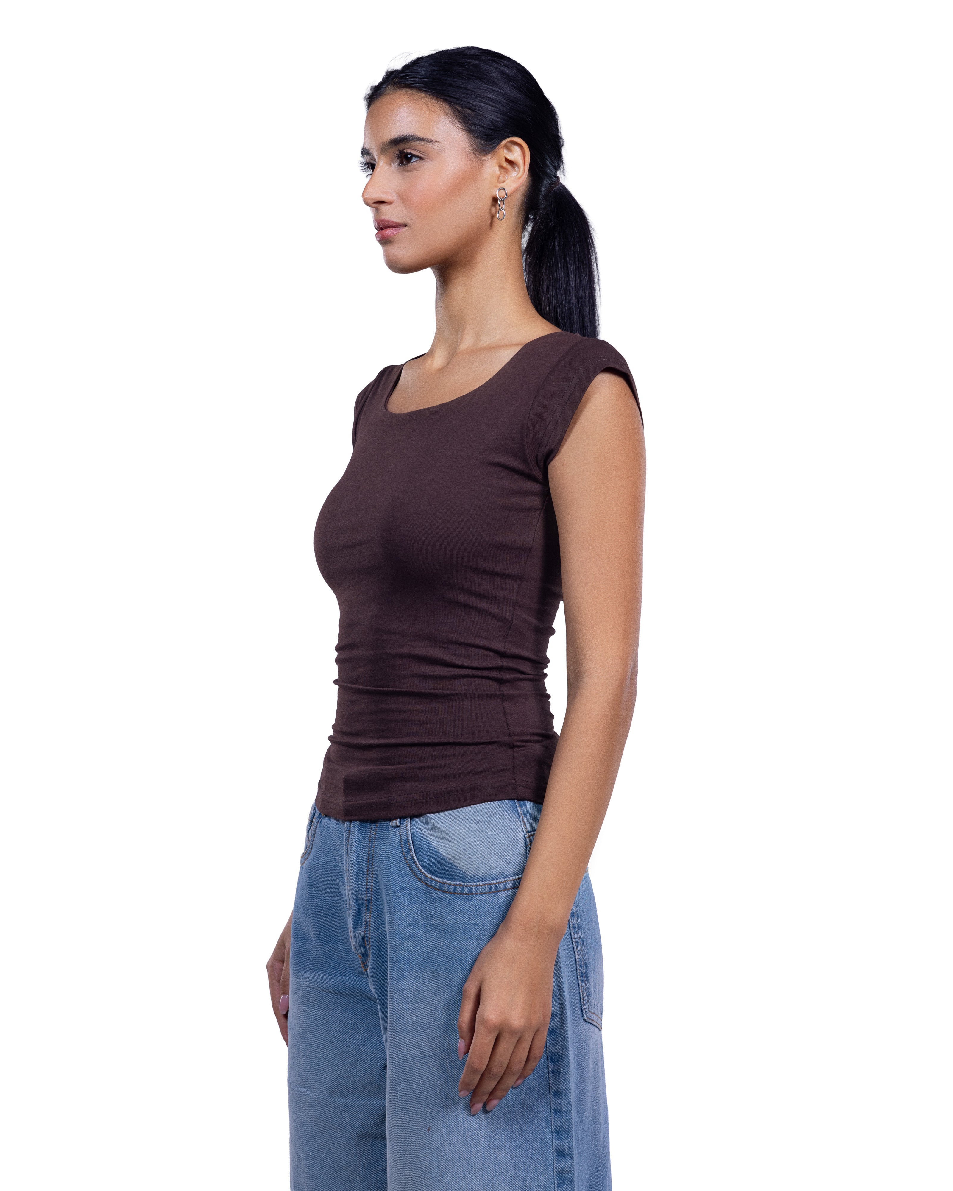 A woman shown in side profile wearing a fitted sleeveless scoop-neck top in dark brown and light-wash blue jeans, photographed against a plain white studio background.