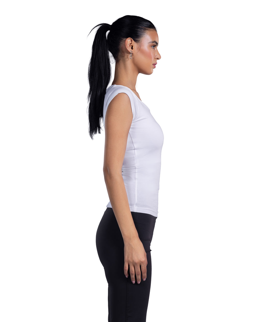 A woman in profile wearing a fitted white sleeveless top and black leggings, standing against a plain white background.