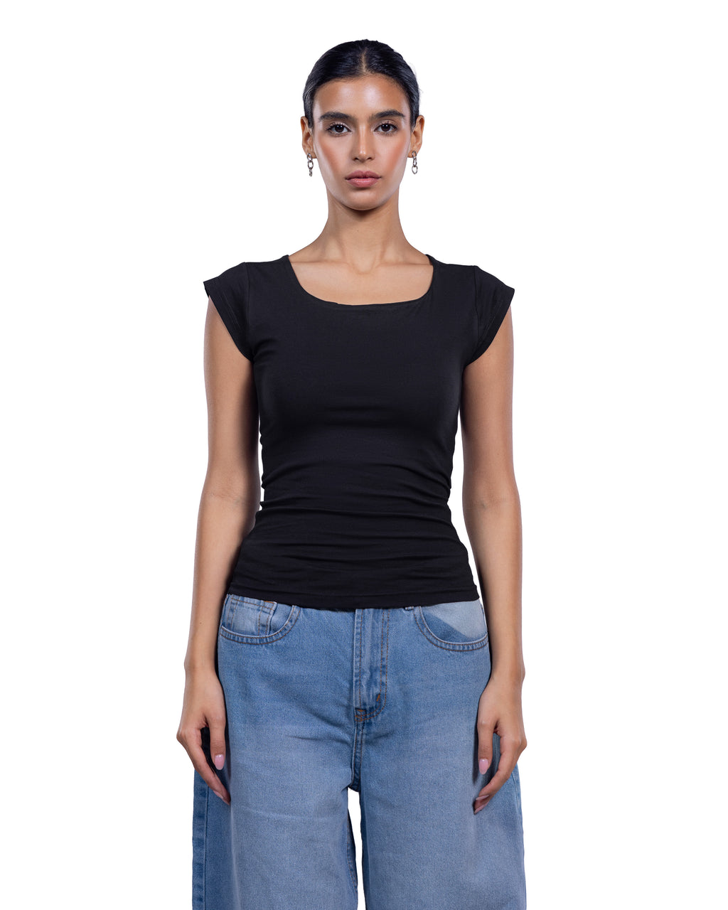 A woman modeling a black short-sleeve scoop-neck top paired with light blue jeans against a plain white background.