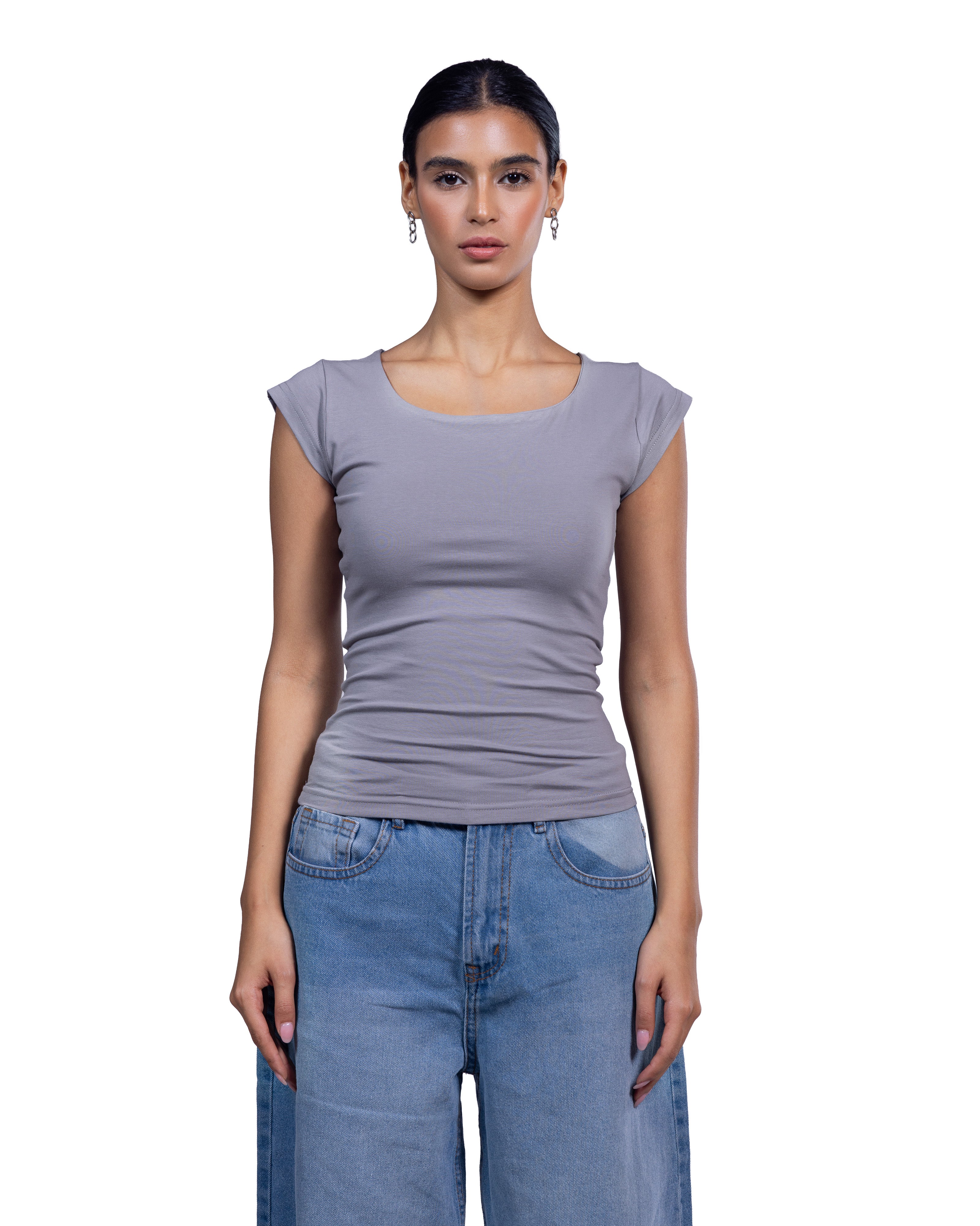 A woman modeling a fitted scoop-neck top with cap sleeves in a dusty lavender-gray color, paired with light-wash blue jeans, against a plain white background.
