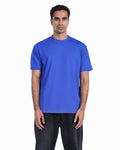 A man wearing a solid royal blue short-sleeve crewneck t-shirt and dark gray pants, standing against a plain white background.