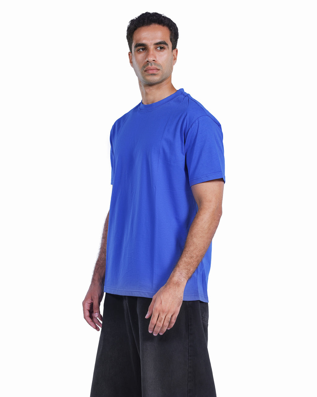 A man wearing a solid royal blue short-sleeve crewneck t-shirt and black pants, standing against a plain white background.