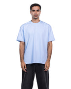 A man modeling a light blue crew-neck t-shirt and black pants against a plain white background.