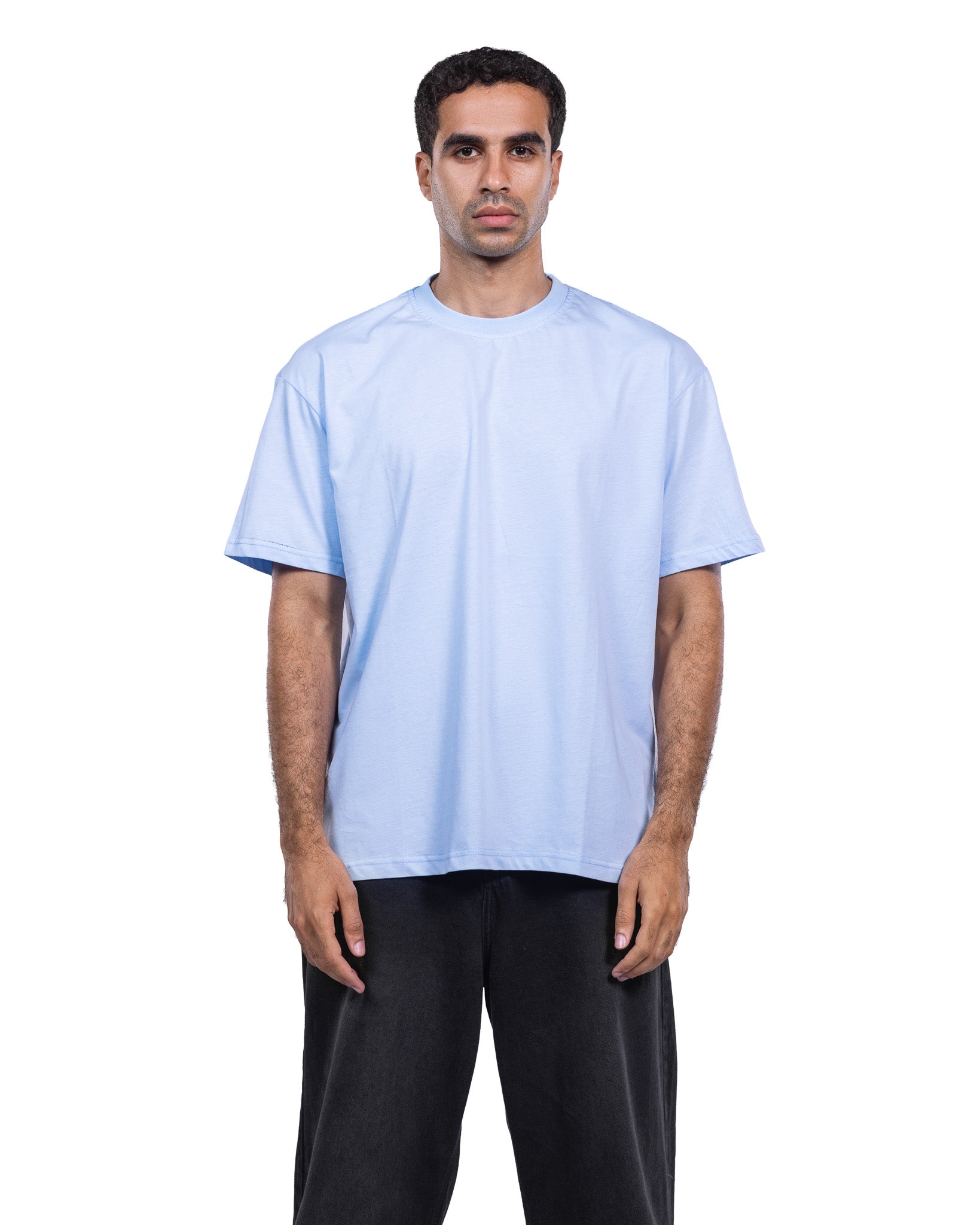 A man modeling a light blue crew-neck t-shirt and black pants against a plain white background.