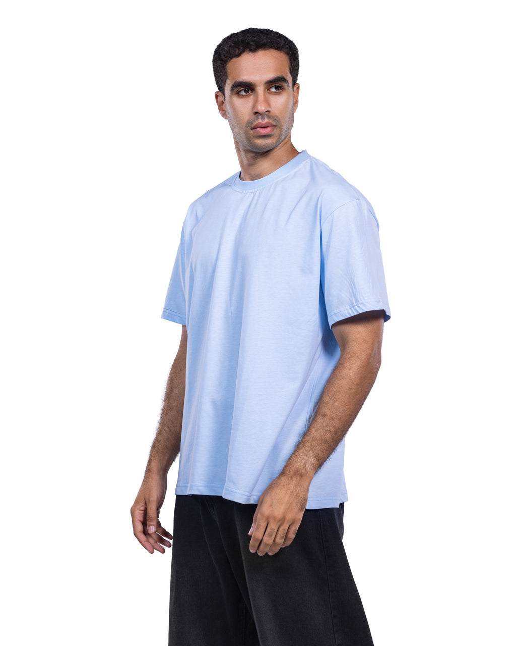 A man wearing a light blue short-sleeve crewneck t-shirt and black pants, standing against a solid white background.