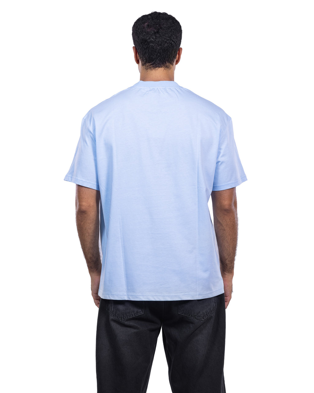 A man viewed from behind wearing a light blue crewneck t-shirt and black pants, shot against a solid white background.