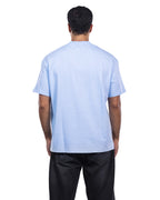 A man viewed from behind wearing a light blue crewneck t-shirt and black pants, shot against a solid white background.