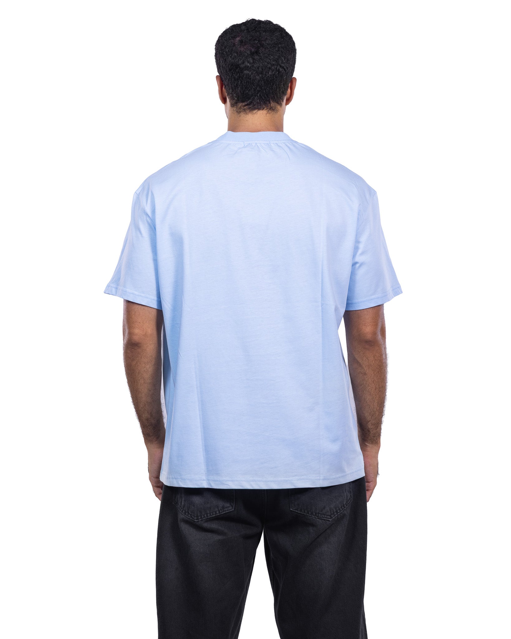 A man viewed from behind wearing a light blue crewneck t-shirt and black pants, shot against a solid white background.