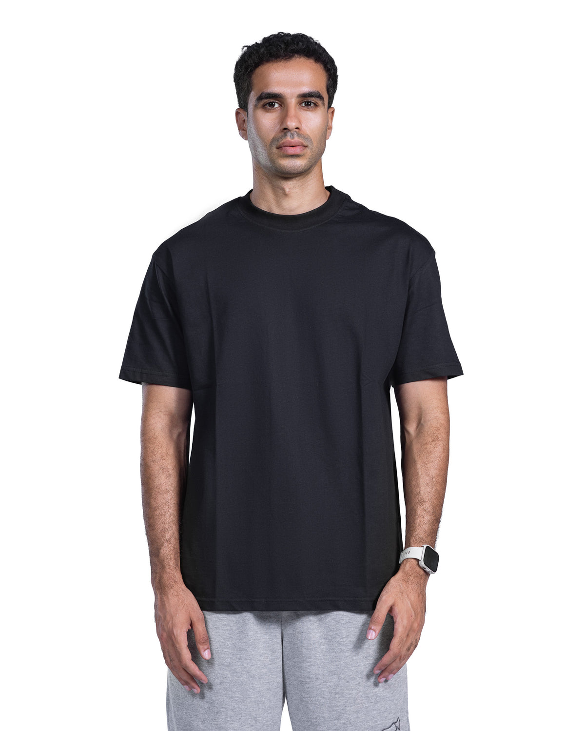 A man wearing a plain black short-sleeve crewneck t-shirt and light gray sweatpants, standing against a solid white background.