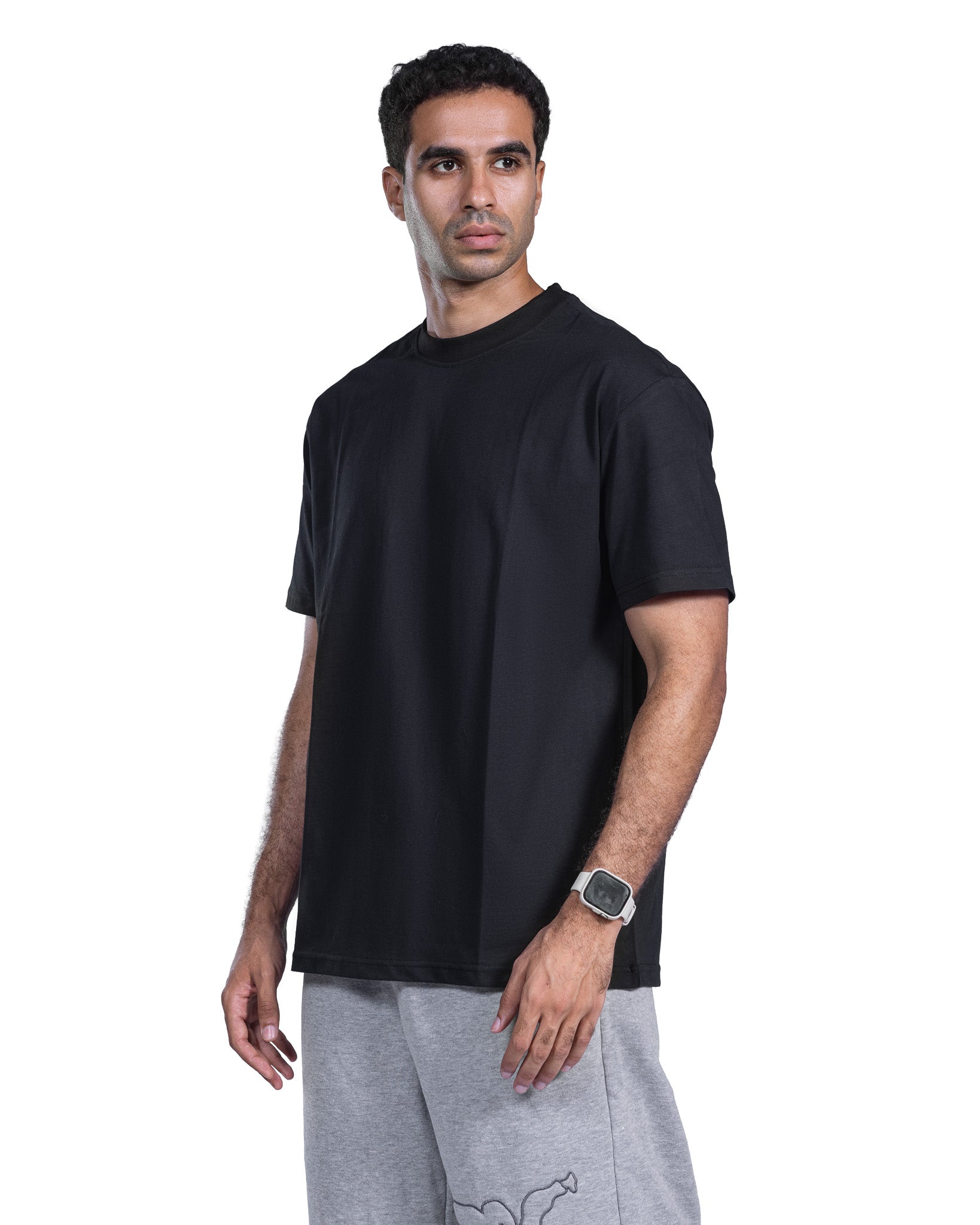A man wearing a plain black short-sleeve crewneck t-shirt and light gray sweatpants, standing against a solid white background.