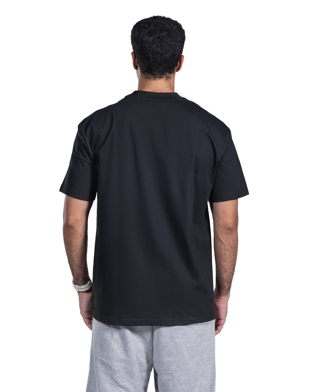 A man viewed from behind wearing a plain black short-sleeve t-shirt and light gray sweatpants against a white background.