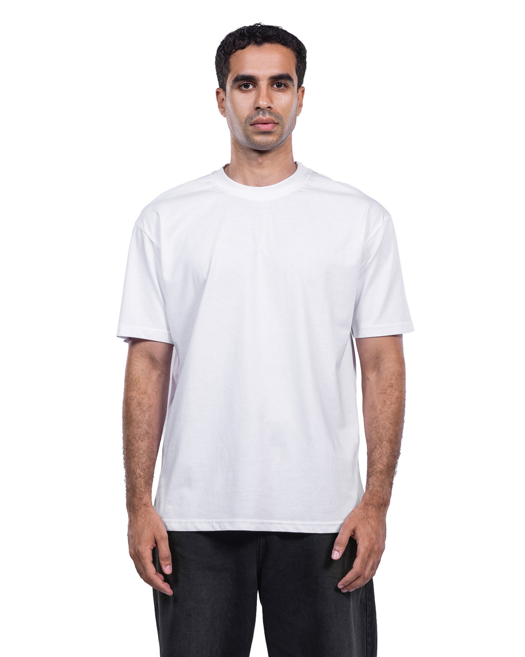 A man wearing a plain white short-sleeve crewneck t-shirt and black pants, standing against a solid white background.