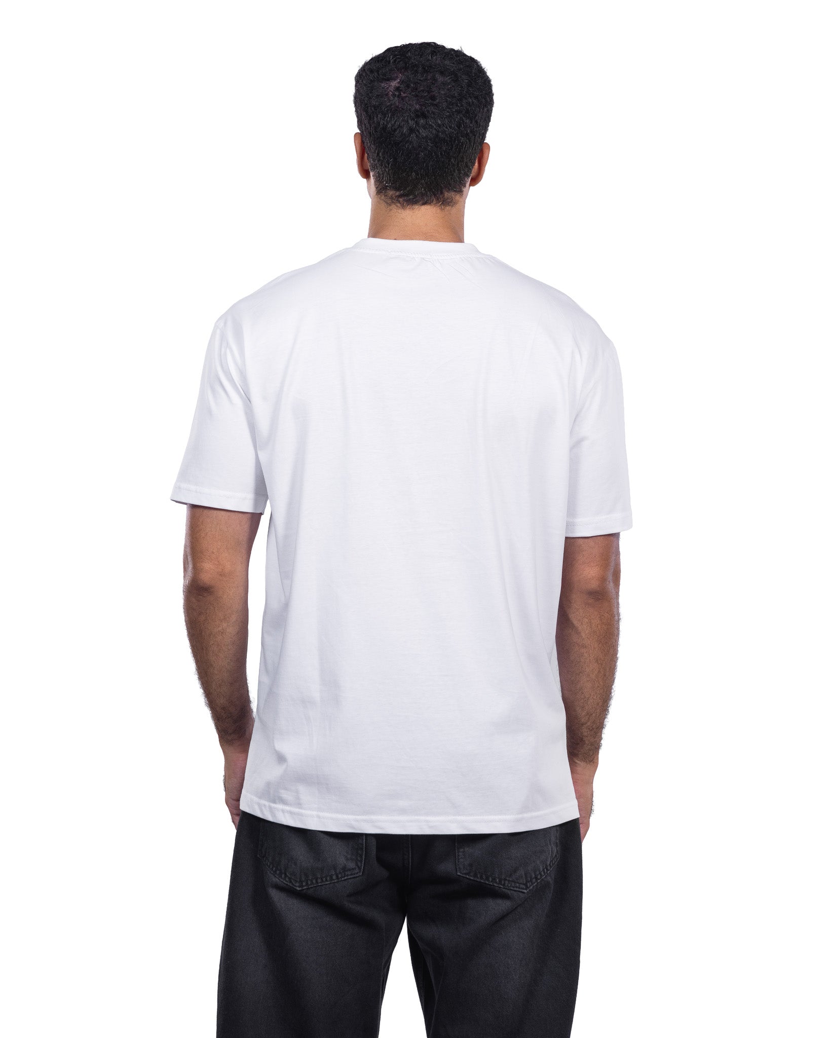 A man viewed from behind wearing a plain white short-sleeve crewneck t-shirt and black jeans, shot against a solid white background.