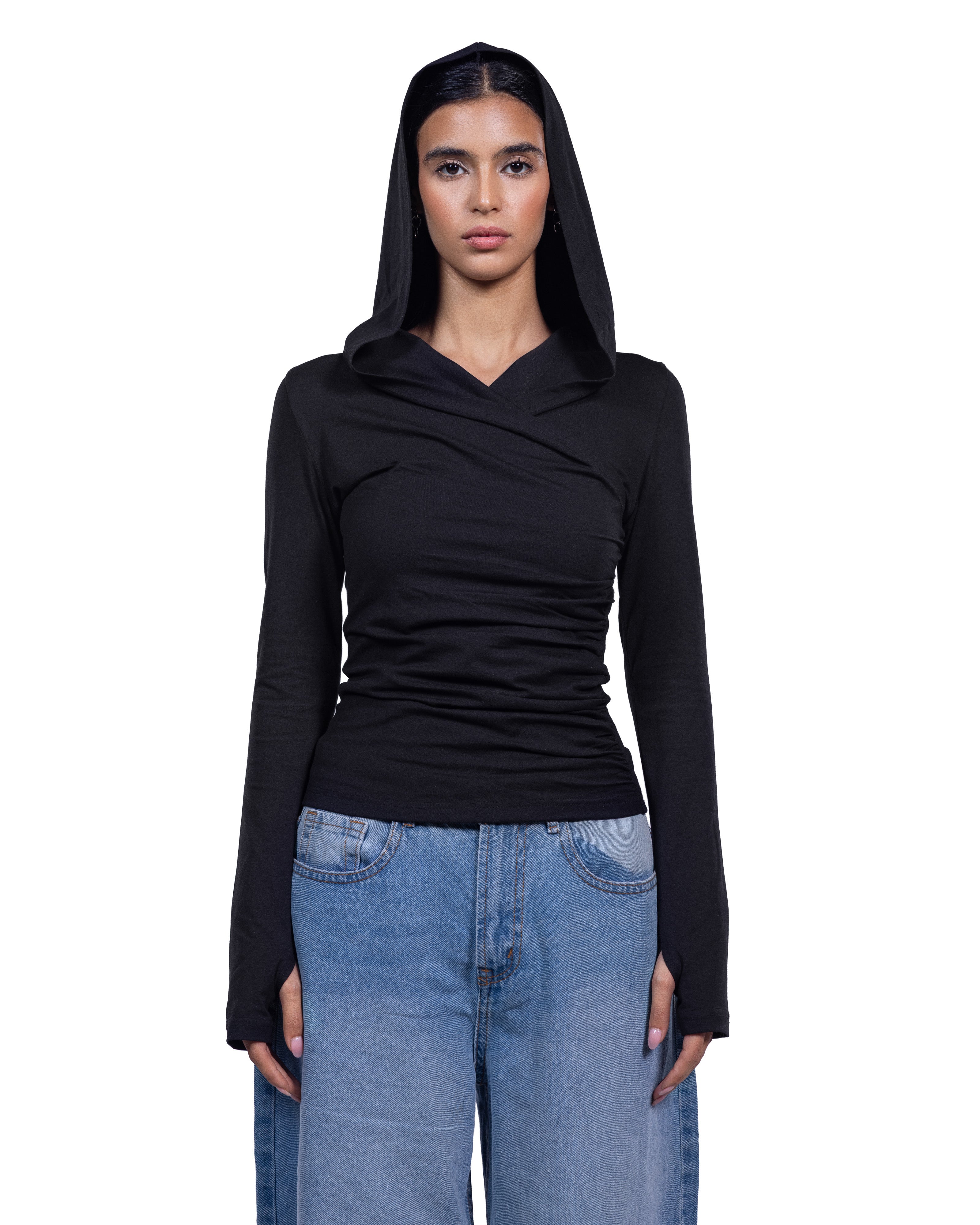 A model wearing a black long-sleeve ruched top with a draped neckline and matching black hood, paired with light blue jeans, against a plain white background.