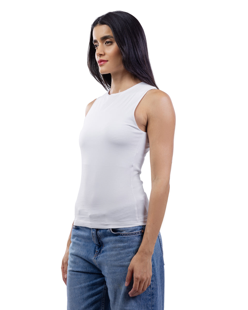 A woman with long dark hair is shown in profile wearing a fitted sleeveless white top and blue jeans against a plain white studio background.