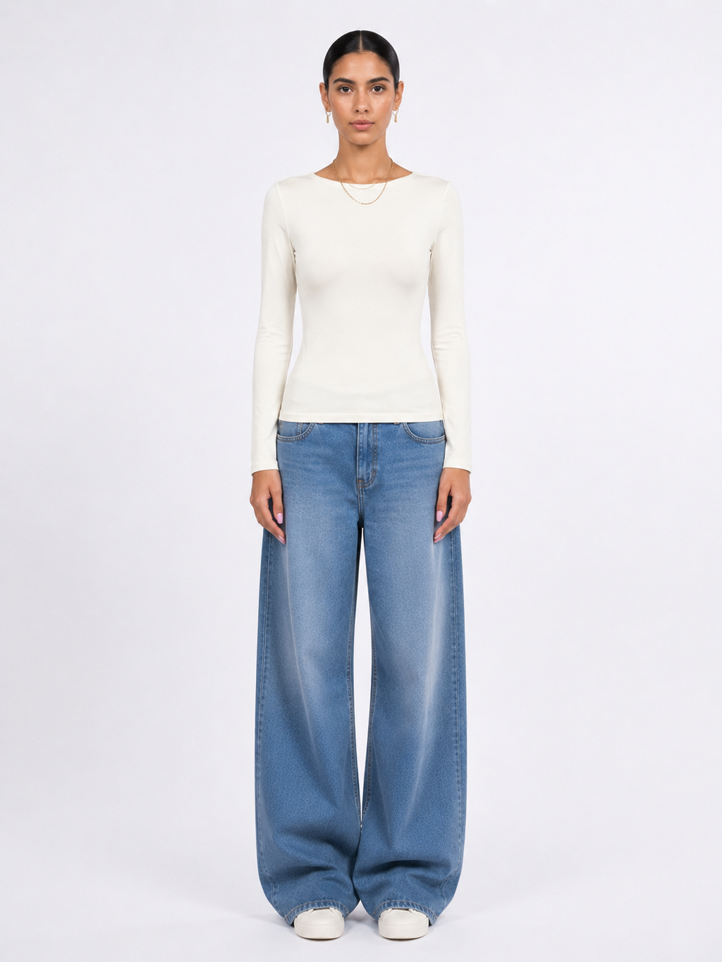 A model stands against a plain white studio background wearing a fitted off-white long-sleeve top, wide-leg light blue jeans, and white shoes. [model:1]