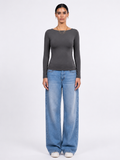 A model stands against a light gray studio background wearing a dark gray long-sleeve boat-neck top and wide-leg light blue jeans.