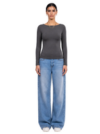 A model stands against a light gray studio background wearing a dark gray long-sleeve boat-neck top and wide-leg light blue jeans. [model:1]