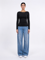 A model stands against a plain white studio background wearing a fitted black long-sleeve top, wide-leg light blue jeans, and white sneakers. [model:1]