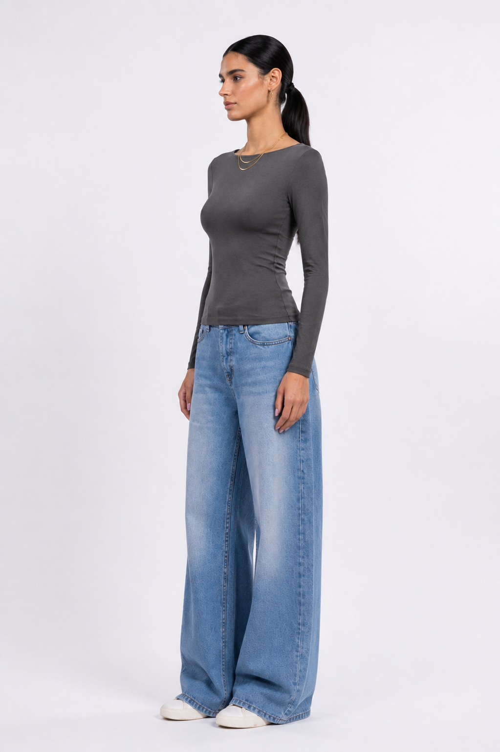 A woman modeling a dark gray long-sleeve top and wide-leg light blue jeans against a plain white studio background.