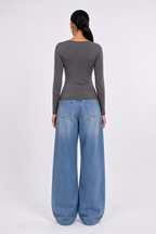 A woman shown from the back wearing a dark gray long-sleeve top and wide-leg light blue denim jeans against a plain light gray studio background. [model:1]