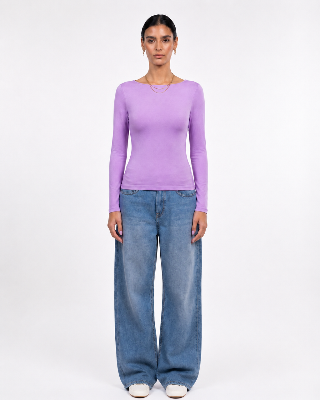 A model stands against a plain white studio background wearing a fitted lavender long-sleeve top and wide-leg blue jeans. [model:1]