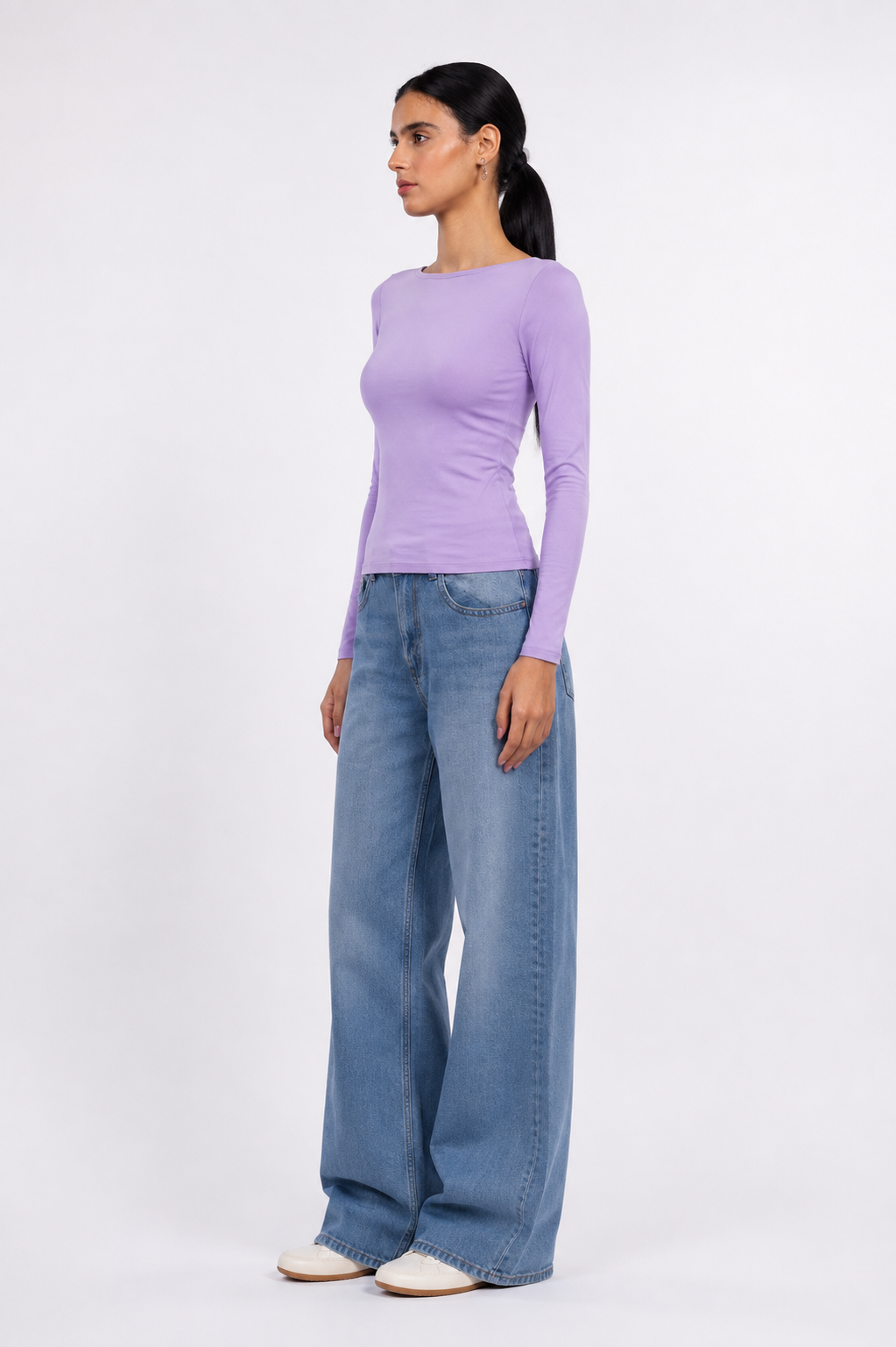 A woman modeling a light purple long-sleeve top and wide-leg blue jeans against a plain white studio background.