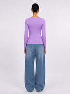 A model viewed from the back wearing a fitted lavender long-sleeve top and wide-leg blue jeans against a plain light gray studio background. [model:1]