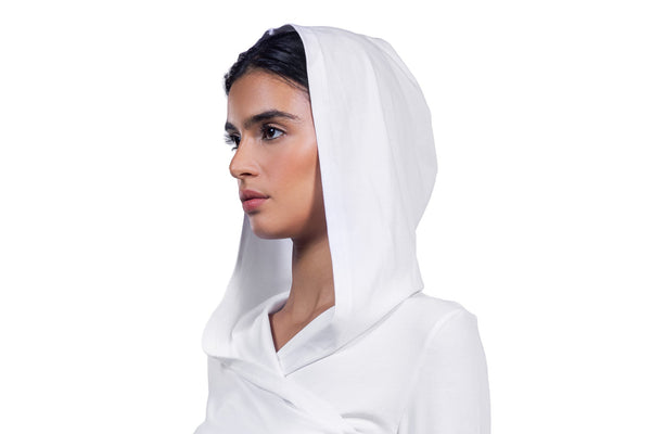 A woman wearing a white hooded garment, shown in profile against a plain white background.